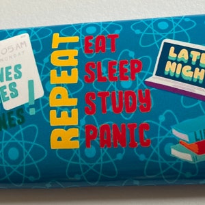 Puede incluir: Un estuche para lápices azul con un patrón repetido de átomos. El estuche tiene un diseño amarillo y rojo con las palabras "REPEAT", "EAT", "SLEEP", "STUDY", "PANIC", "DEADLINES", "LATE NIGHT" y "LIBRARY".