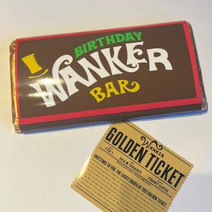 May include: A novelty chocolate bar with the text "BIRTHDAY WANKER BAR" in white and yellow on a brown wrapper. A "Golden Ticket" is also present, with text in black on a gold background.