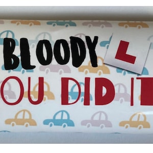 May include: A white chocolate bar with a colorful car pattern and the text "BLOODY YOU DID IT!" with a red L-shaped sign.