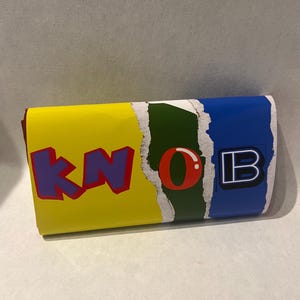 May include: A yellow, green and blue box with the word "KNOB" printed on it in colourful letters.