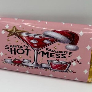 Op de afbeelding: Roze chocoladereepverpakking met gouden folieranden. De verpakking toont een afbeelding van een cocktail, een kerstmuts en de tekst "Santa's Hot Favorite Mess". Een gouden ster en diamanten staan ook op de verpakking.
