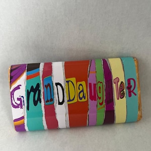 Op de afbeelding: Een kleurrijke chocolade reep met het woord "Granddaughter" gespeld in verschillende gekleurde stroken.