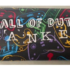 Puede incluir: Un objeto rectangular negro con un patrón de mandos de videojuegos coloridos y las palabras "CALL OF DUTY WANKER" en blanco. Los mandos están delineados en varios colores.