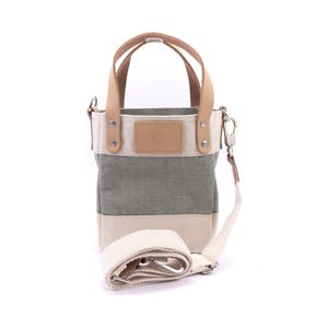 May include: A small, green and white striped canvas tote bag with a leather handle and a detachable shoulder strap. The bag has a small leather patch with a logo on the front.