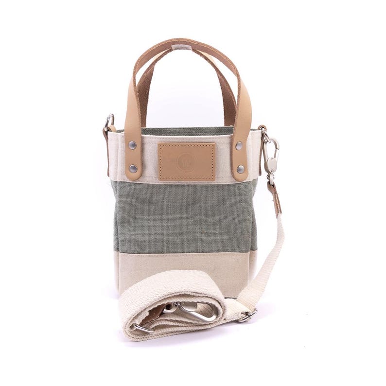May include: A small, green and white striped canvas tote bag with a leather handle and a detachable shoulder strap. The bag has a small leather patch with a logo on the front.