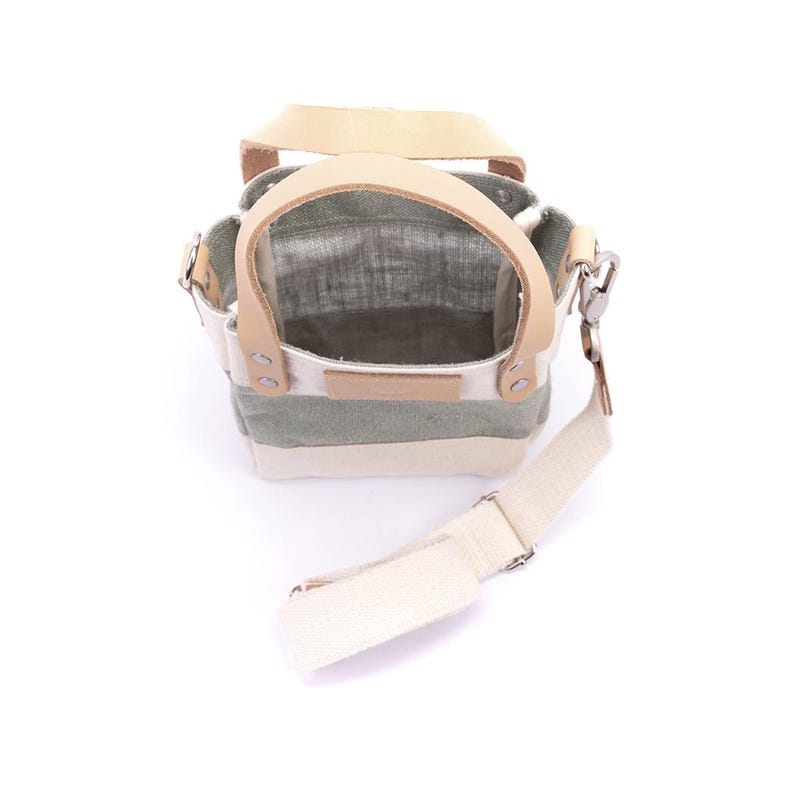 May include: A small, striped canvas tote bag with a tan leather handle and a long, adjustable strap. The bag is open and empty, showing the interior lining.