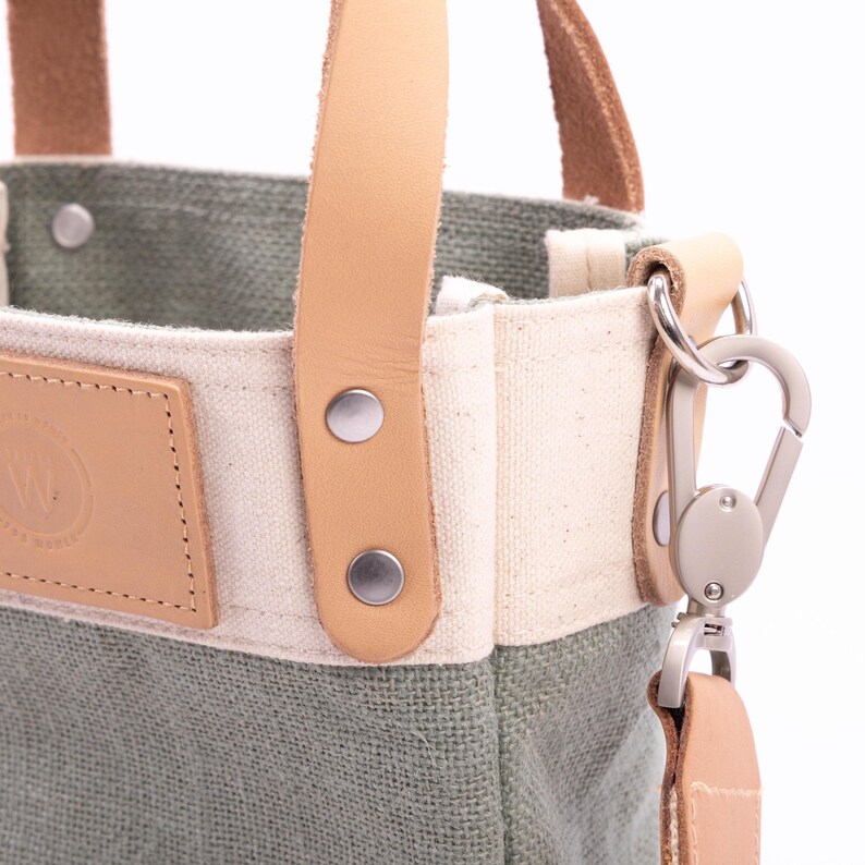 May include: A small green canvas tote bag with tan leather handles and a metal clasp. The bag has a white canvas panel with a tan leather patch.