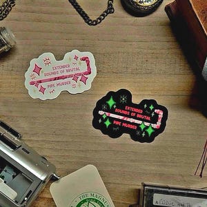 May include: Two stickers with the text "Extended Sounds of Brutal Pipe Murder" in pink and white, and black and green. A vintage cassette player, a glass bottle with contents, and a leather-bound book are also visible on a wooden surface.