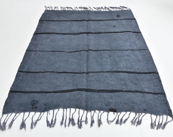 May include: A rectangular, dark gray rug with horizontal black stripes. The rug has a fringed edge and appears to be made of a woven material. The rug is displayed on a white surface.