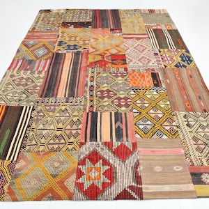 May include: A large, rectangular patchwork rug with a variety of geometric and striped patterns in shades of brown, red, orange, yellow, and cream. The rug is made up of numerous individual pieces sewn together.