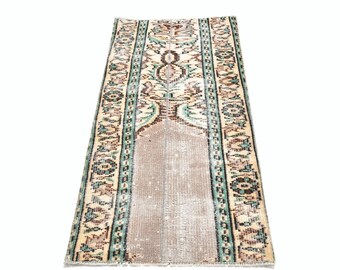 May include: Rectangular rug with a central beige field and a patterned border. The rug features a beige, brown, and teal color palette with floral and geometric designs. The rug is likely made of woven material.