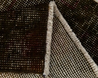 May include: Close-up of a dark brown and white patterned rug. The rug has a woven texture with small white dots scattered across the dark brown background. The edge of the rug is visible, with a fringed border.
