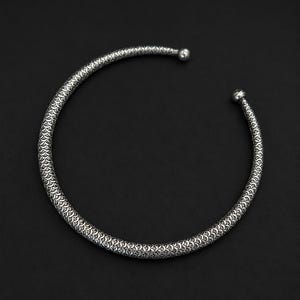 Peut inclure: Un collier ras du cou argent&eacute; avec un motif textur&eacute; en forme d'&eacute;cailles. Le design ouvert pr&eacute;sente une petite boule &agrave; chaque extr&eacute;mit&eacute;. Le collier est pos&eacute; sur un fond sombre, soulignant ses d&eacute;tails complexes et son &eacute;clat m&eacute;tallique.