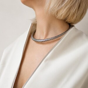 Peut inclure: Un collier ras du cou argent&eacute; avec une surface textur&eacute;e. Le collier est port&eacute; sur une veste blanche avec une fermeture &eacute;clair. Le mod&egrave;le a les cheveux blonds courts.