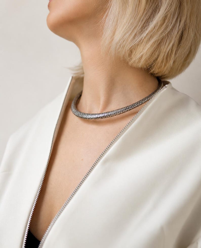 Peut inclure: Un collier ras du cou argent&eacute; avec une surface textur&eacute;e. Le collier est port&eacute; sur une veste blanche avec une fermeture &eacute;clair. Le mod&egrave;le a les cheveux blonds courts.