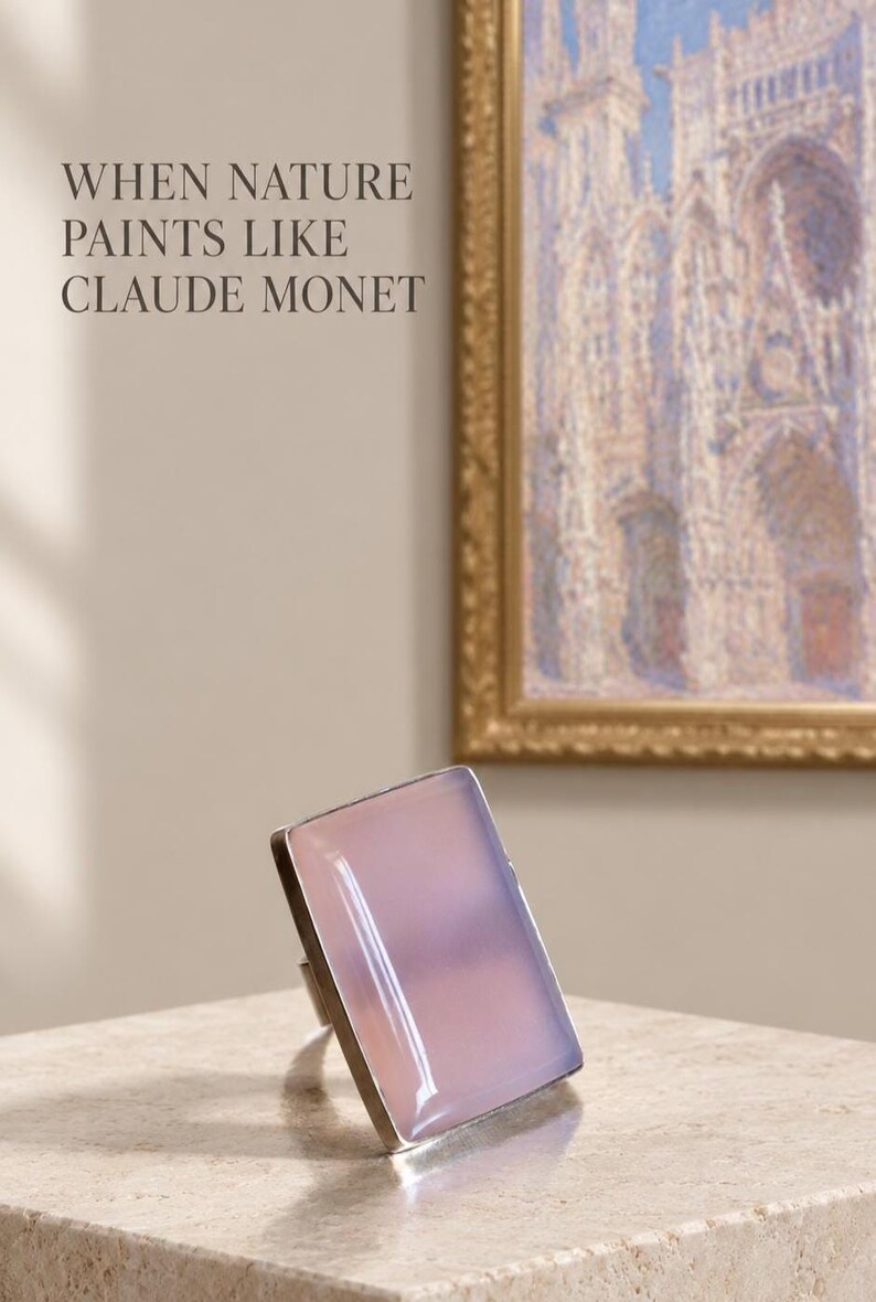 Pu&ograve; includere: Un anello rettangolare con una pietra liscia, traslucida e rosa pallido incastonata in una montatura in metallo argentato. Il testo "WHEN NATURE PAINTS LIKE CLAUDE MONET" &egrave; visibile nell'angolo in alto a sinistra, sopra un quadro incorniciato.