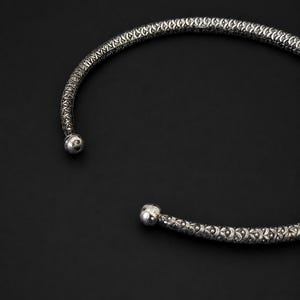 Peut inclure: Un collier ras du cou argent&eacute; avec un motif textur&eacute;. Le collier a une forme arrondie avec une petite boule &agrave; chaque extr&eacute;mit&eacute;. Le fond est noir uni.