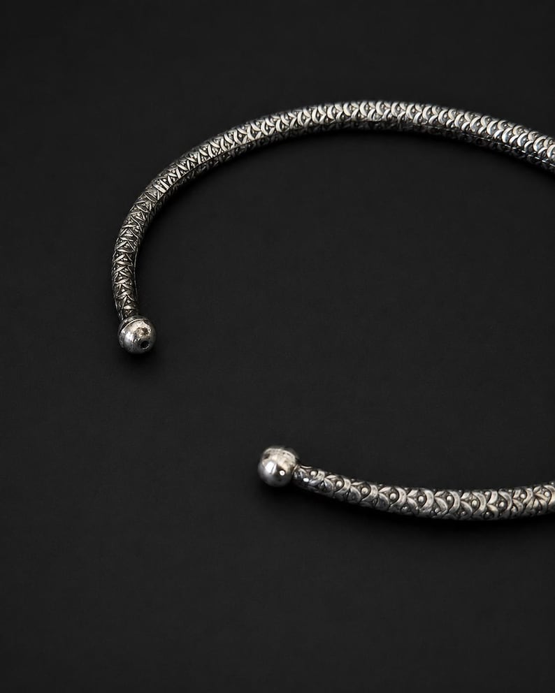 Peut inclure: Un collier ras du cou argent&eacute; avec un motif textur&eacute;. Le collier a une forme arrondie avec une petite boule &agrave; chaque extr&eacute;mit&eacute;. Le fond est noir uni.