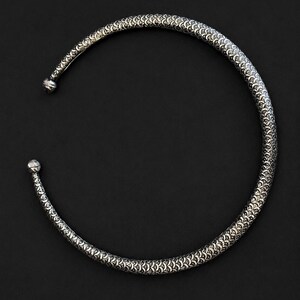 Peut inclure: Un collier ras du cou argent&eacute; avec un motif textur&eacute; en forme d'&eacute;cailles. Le collier a une forme arrondie avec une petite boule &agrave; chaque extr&eacute;mit&eacute;. Le fond est noir uni.