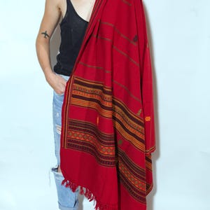 May include: A vibrant red shawl with intricate geometric patterns in shades of orange, brown, and green. The shawl features a fringed edge and is draped over the shoulders. The textile is a warm, cozy accessory.
