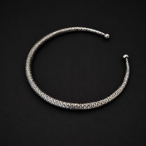 Peut inclure: Un collier ras du cou argent&eacute; avec un motif textur&eacute; et d&eacute;taill&eacute;. Le collier a une forme arrondie et se r&eacute;tr&eacute;cit aux extr&eacute;mit&eacute;s, avec de petites fermetures en forme de boule. Le fond est noir uni.