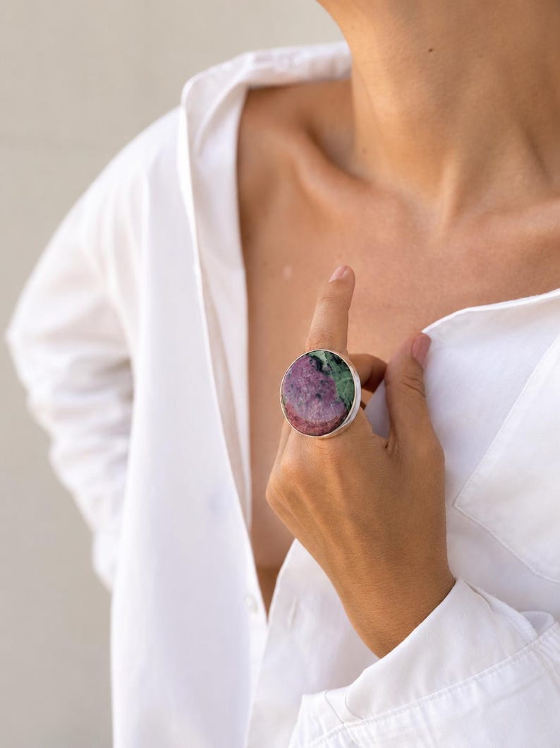 Puede incluir: Un anillo llamativo con una piedra preciosa grande y redonda en tonos rosa, verde y blanco, engastada en una banda plateada. El anillo es una pieza de joyer&iacute;a audaz, adecuada para moda o como elemento decorativo.