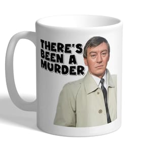 May include: White ceramic mug with the text "THERE'S BEEN A MURDER" in black, and an image of a man in a light-coloured coat. The mug has a curved handle and is suitable for hot or cold drinks.