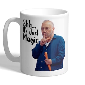 May include: White ceramic mug with a man in a blue shirt holding a carrot and gesturing for silence. The mug features the text "Shh... It's Just Magic" in black script.