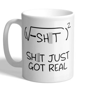 May include: A white ceramic mug featuring a black printed mathematical equation that reads (√-SH*T)² followed by the text SH*T JUST GOT REAL. The design includes a handle on the left side and a cylindrical body with a smooth, glossy finish.