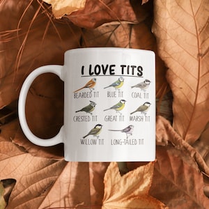 May include: White ceramic mug with a black and white image of different types of birds. The text "I LOVE TITS" is printed in black at the top of the mug. Below the text are the names of the birds: Bearded Tit, Blue Tit, Coal Tit, Crested Tit, Great Tit, Marsh Tit, Willow Tit, and Long-tailed Tit.