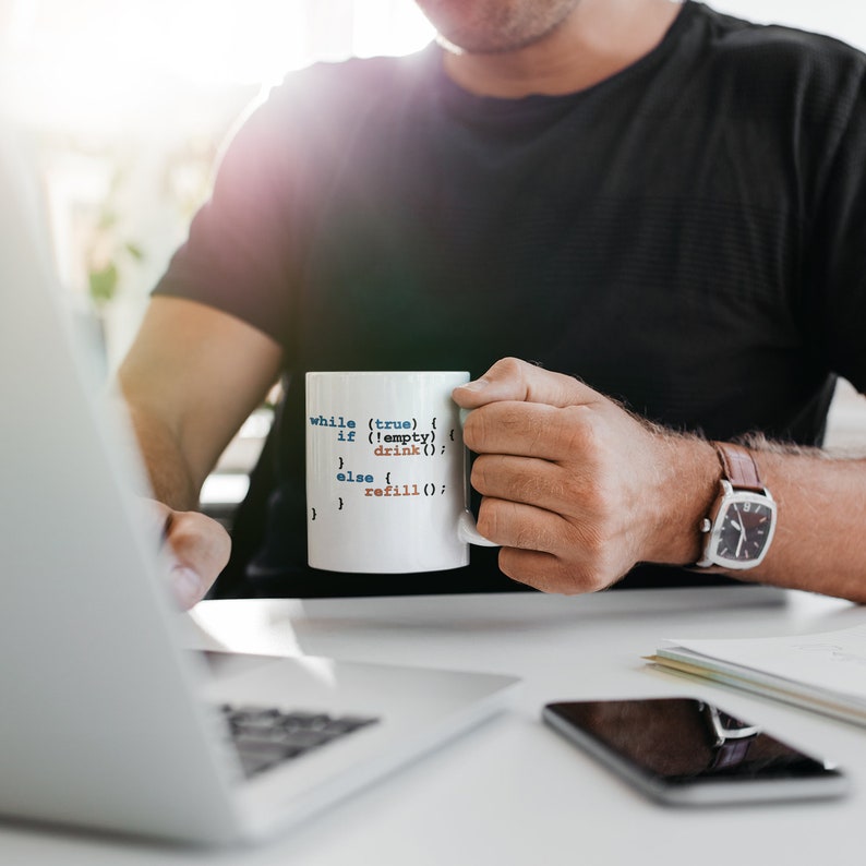 K&ouml;nnte beinhalten: Eine wei&szlig;e Keramiktasse mit einem darauf gedruckten Code, der "while (true) { if (!empty) { drink(); } else { refill(); } }" lautet. Die Tasse wird von einer Person gehalten, die ein schwarzes T-Shirt und eine Uhr tr&auml;gt.