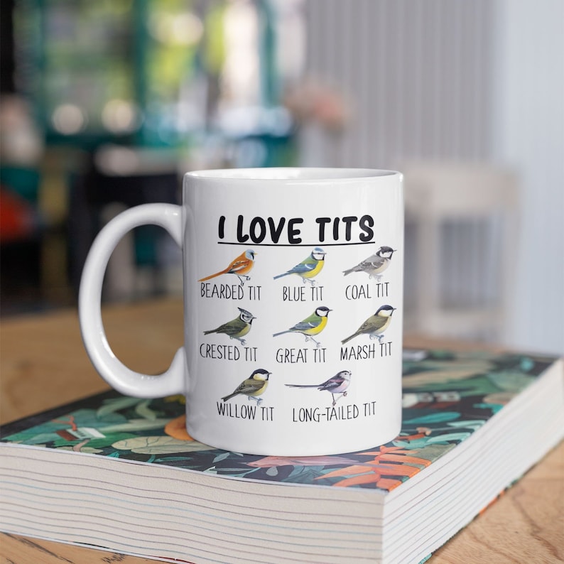 May include: White ceramic mug with a black graphic that says "I LOVE TITS" and features illustrations of different types of birds with their names listed below them: Bearded Tit, Blue Tit, Coal Tit, Crested Tit, Great Tit, Marsh Tit, Willow Tit, Long-tailed Tit.