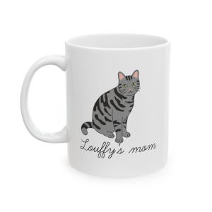 Op de afbeelding: Witte keramische mok met een grijze tabby kat illustratie en de tekst "Louffy's mom". De kat heeft groene ogen en zwarte strepen. De mok heeft een gebogen handvat.