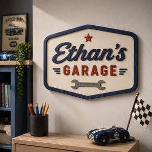 Könnte beinhalten: Ein Wandschild mit cremefarbenem Hintergrund und dunkelblauem Rand. Der Text lautet Ethan's in blauer Schreibschrift und GARAGE in roten Blockbuchstaben. Ein kleiner roter Stern befindet sich darüber und ein grauer Schraubenschlüssel unten.