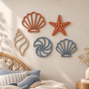 Peut inclure: Un ensemble de cinq décorations murales comprenant un coquillage en forme de coquille Saint-Jacques terracotta, une étoile de mer terracotta à points en relief, un coquillage beige clair, un nautile bleu et une coquille Saint-Jacques bleue.