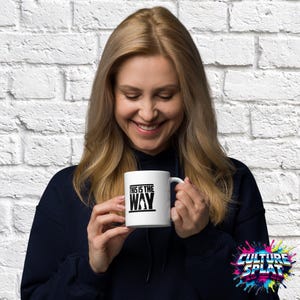 May include: A white ceramic mug featuring a black graphic print with the text "THIS IS THE WAY" and a silhouette of a character. The mug has a standard handle and a smooth finish, designed for holding hot or cold beverages in a simple, functional style.