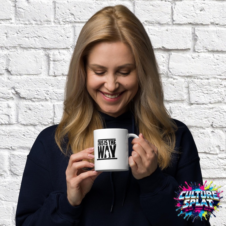 May include: A white ceramic mug featuring a black graphic print with the text "THIS IS THE WAY" and a silhouette of a character. The mug has a standard handle and a smooth finish, designed for holding hot or cold beverages in a simple, functional style.