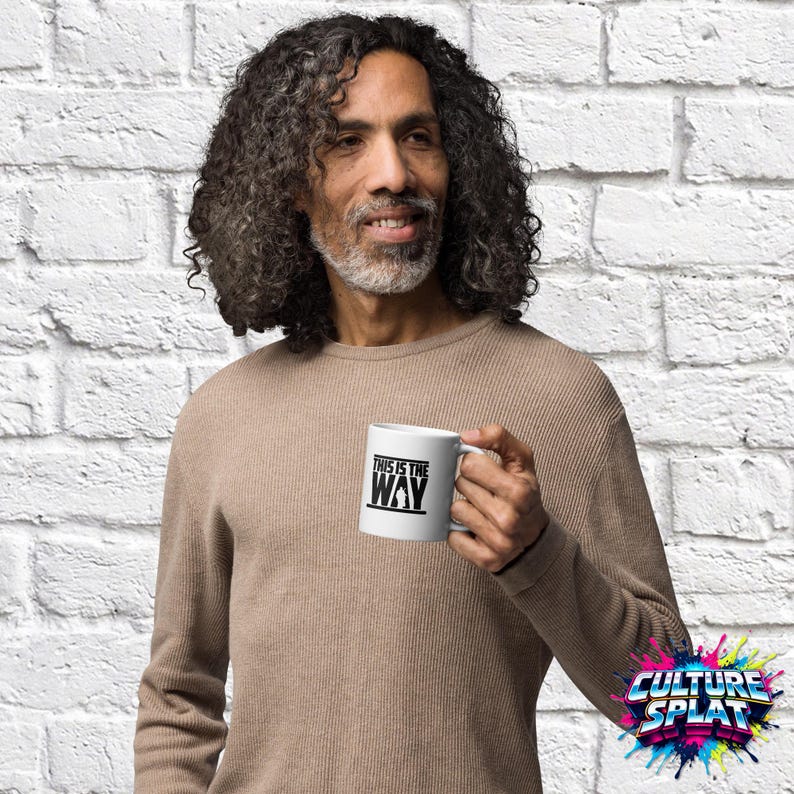 May include: A white ceramic mug featuring the black text "THIS IS THE WAY" printed on the side, accompanied by a small black silhouette graphic of a figure. The mug has a standard handle and a smooth, cylindrical body design.