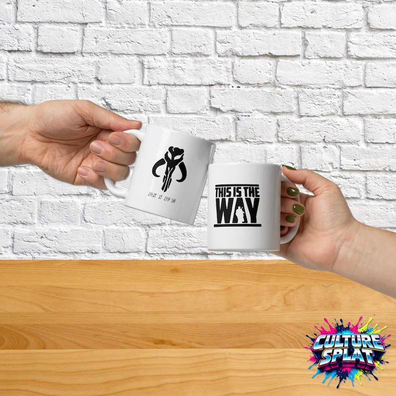 May include: Two white ceramic mugs featuring black graphic designs. One mug displays a black Mythosaur skull icon with the text "THIS IS THE WAY" below it. The second mug features the bold black text "THIS IS THE WAY" with a silhouette figure.