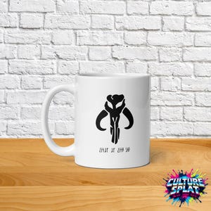 May include: A white ceramic mug featuring a black graphic of a stylized Mandalorian mythosaur skull emblem centered on the front. Below the skull icon, there is a line of black text written in the fictional Aurebesh script from Star Wars.