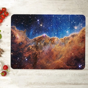 May include: Rectangular placemat featuring a vibrant image of a nebula with a blue and orange color scheme. The placemat is placed on a white wooden surface, alongside fresh seafood and vegetables.