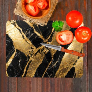 May include: A black and gold marble cutting board with a silver knife and red tomatoes. The cutting board has a decorative pattern of gold veins on a black background.