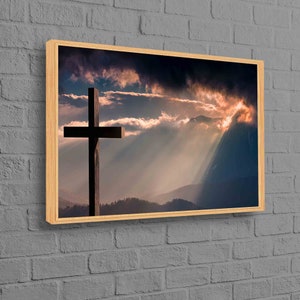May include: A framed print of a wooden cross silhouetted against a mountain range with a dramatic sunset sky. The sky is filled with clouds and rays of light.