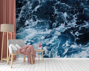 May include: A close-up of a blue and white ocean wave pattern. The wave pattern is used as wallpaper in a room with a chair, a lamp, and a side table.