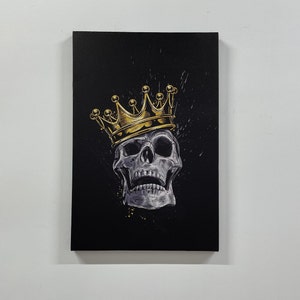 May include: A black canvas print with a white skull wearing a gold crown. The skull has a detailed design and is set against a black background with gold splatters.