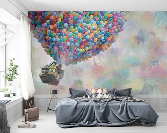 May include: A bedroom with a colorful balloon mural featuring a house floating in the air. The mural is on the wall behind a gray bed with pillows and a blanket.
