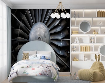 May include: A child's bedroom with a light blue bed and a patterned comforter featuring vehicles and animals. A teddy bear sits on the bed. The wall behind the bed has a large image of a jet engine. A white bookshelf and a beanbag chair are also in the room.