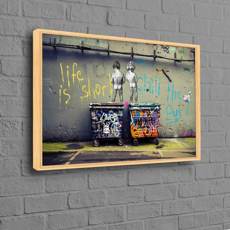 May include: A framed print of a street art piece featuring two children standing in front of two graffiti-covered trash cans. The wall behind them has the words "Life is short, chill the f*** out" written in yellow and blue paint.