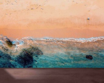 May include: An aerial view of a sandy beach with turquoise water crashing on the shore. The water is clear and blue, with white foam on the waves. The sand is a light brown colour.