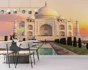 May include: A white marble building with intricate details, known as the Taj Mahal, is the focal point of this image. The building is surrounded by a lush green lawn and a reflecting pool. The sky is a vibrant orange and pink, creating a beautiful sunset backdrop.